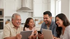 Multicultural family smiling while using technology devices in a modern kitchen.