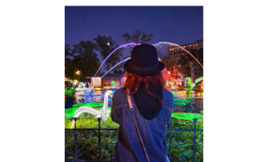 Romina seen from behind admiring the illuminated fountain and colorful lanterns during her night visit to the Philadelphia Chinese Lantern Festival in Franklin Square.