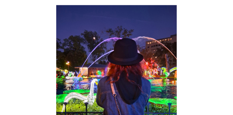 Romina seen from behind admiring the illuminated fountain and colorful lanterns during her night visit to the Philadelphia Chinese Lantern Festival in Franklin Square.